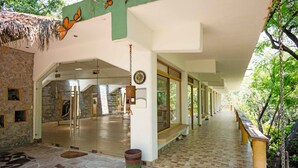 A building with a glass entrance, a wooden bench outside, and a stone floor inside. - Agua Blanca (Jungapeo)