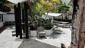 Un patio al aire libre con suelo de baldosas, arreglos de asientos y plantas en macetas.