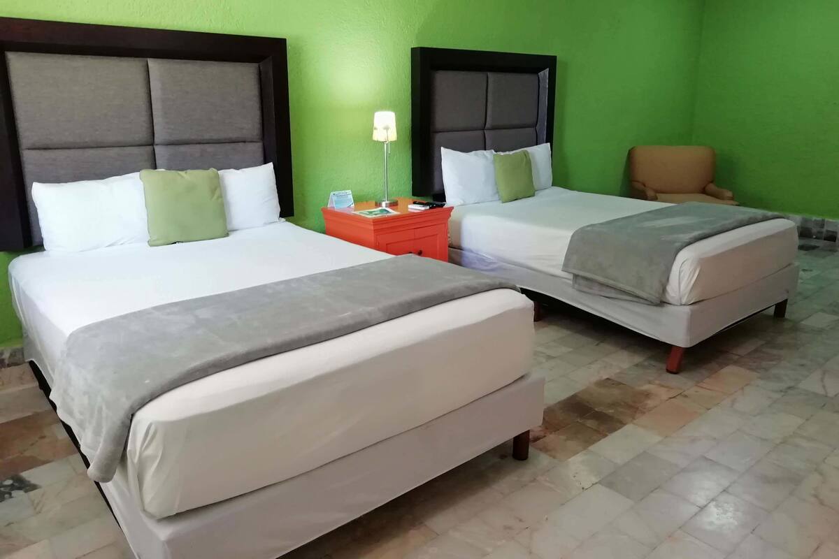 A hotel room with two beds, a nightstand, a chair, and green walls.