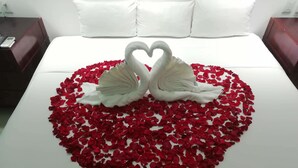 Una cama con un arreglo de pétalos de rosa en forma de corazón y dos toallas con forma de cisne.