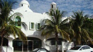 Un edificio blanco con una cúpula y una torre, palmeras y coches aparcados.