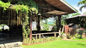 Un espace extérieur abrité, doté d’une structure en bois, d’une végétation luxuriante et d’un panneau indiquant la présence d’un hôtel.