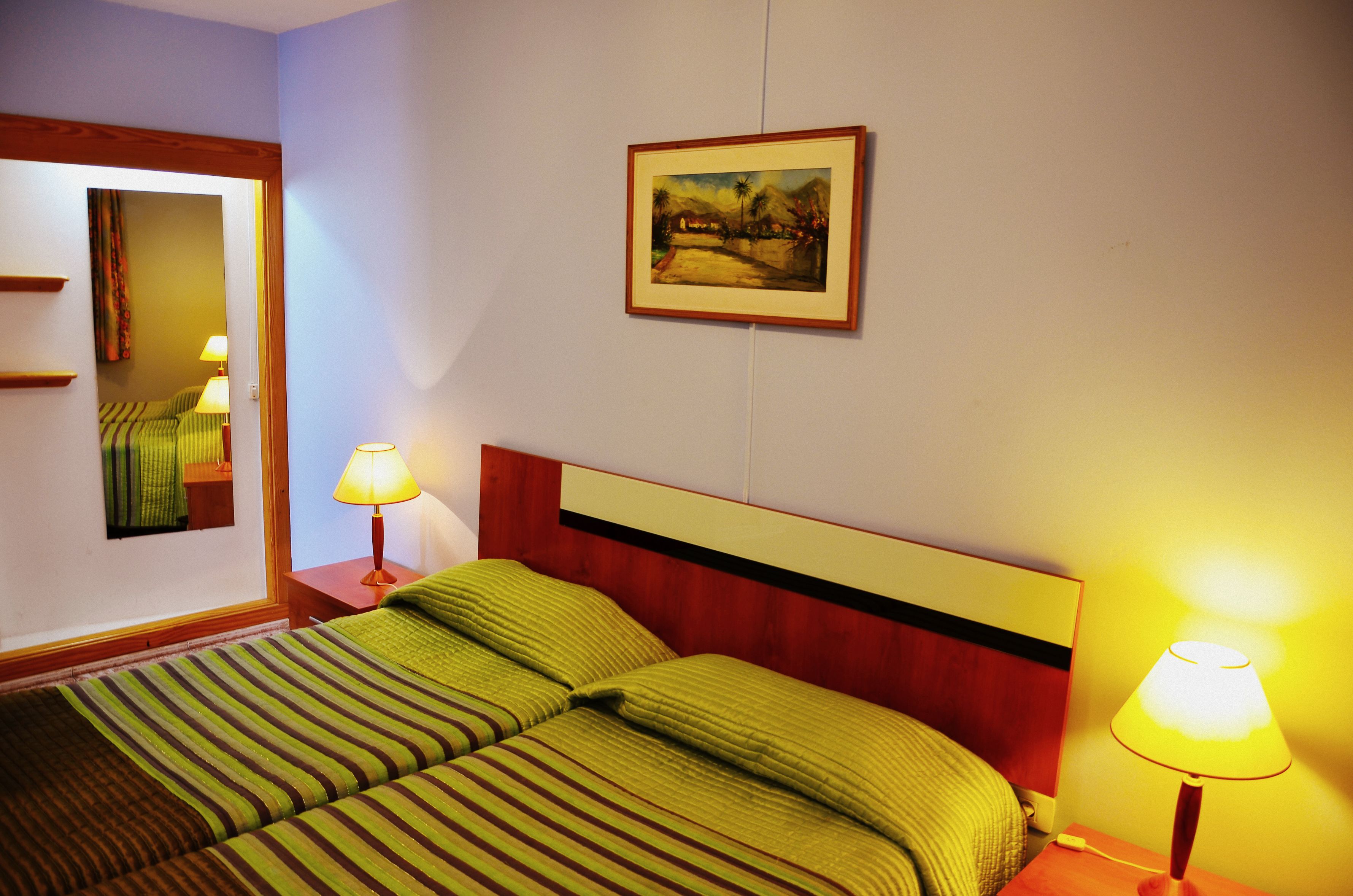 A hotel room with a bed, two bedside lamps, a framed picture on the wall, and a mirror on the wall.