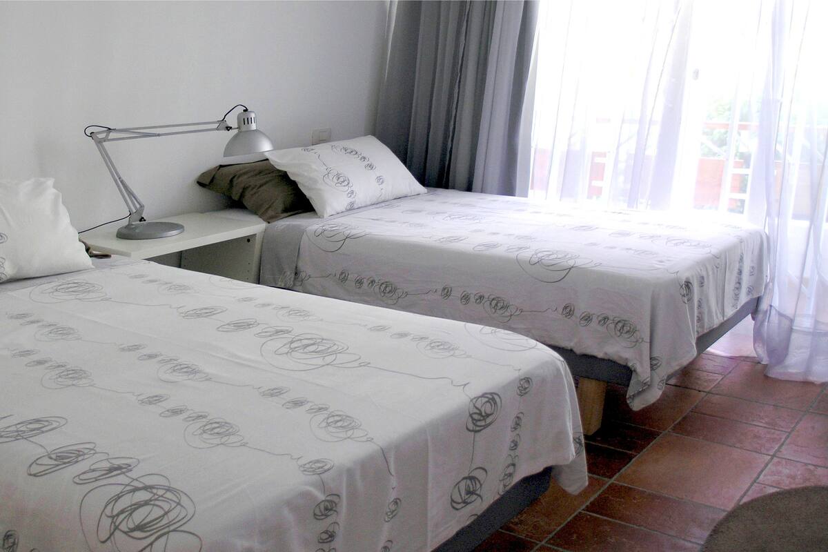 Ein Hotelzimmer mit zwei Betten, einem Schreibtisch mit Lampe und einem Fenster mit Vorhängen.