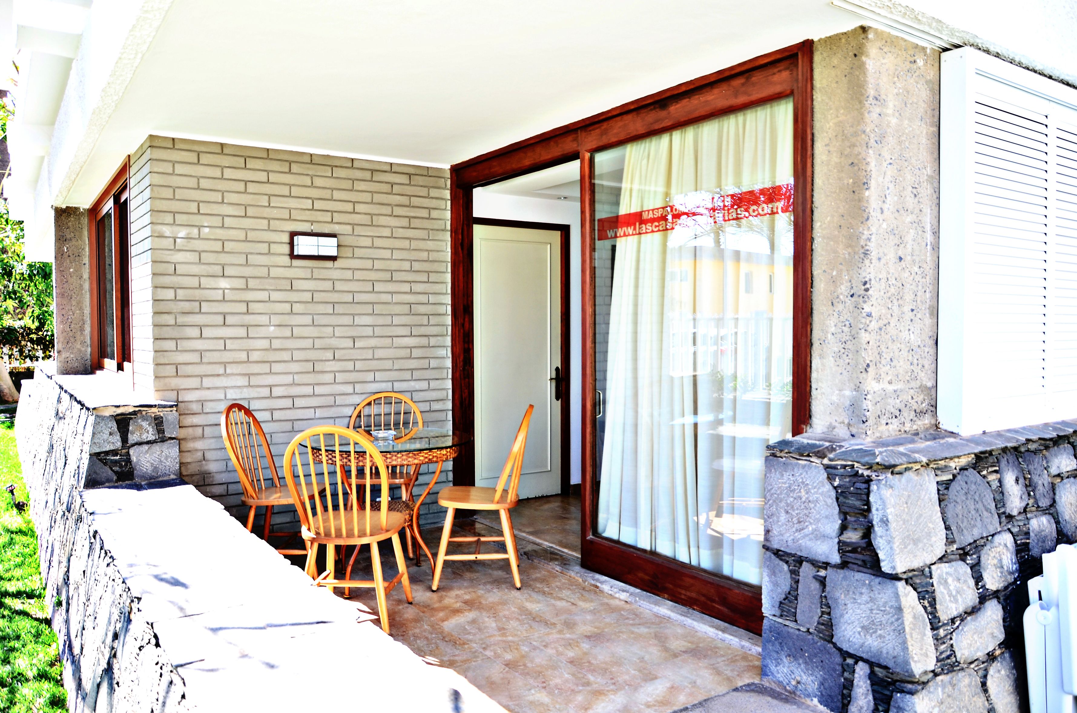 Un patio con tavolo e sedie, un muro in pietra e una porta scorrevole in vetro.