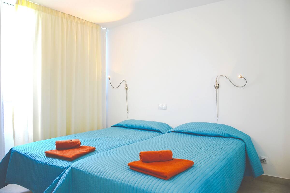 Ein Zimmer mit zwei Betten, jeweils mit blauer Bettdecke und orangefarbenen Kissen.