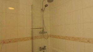 Cabina de ducha con paredes de vidrio, cabezal de ducha de mano y grifo montado en la pared.