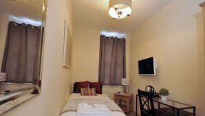 Una habitación de hotel con cama, mesita de noche, silla, escritorio, televisor y cortinas.