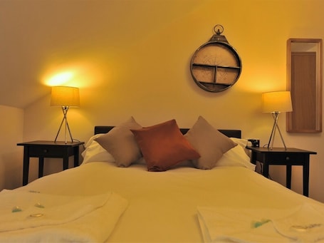 A hotel room with a bed, two bedside tables with lamps, a round wall clock, and a door.