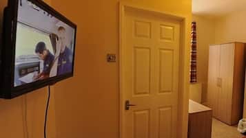 A room with a television mounted on the wall displaying a scene, a closed door, and a wooden wardrobe.