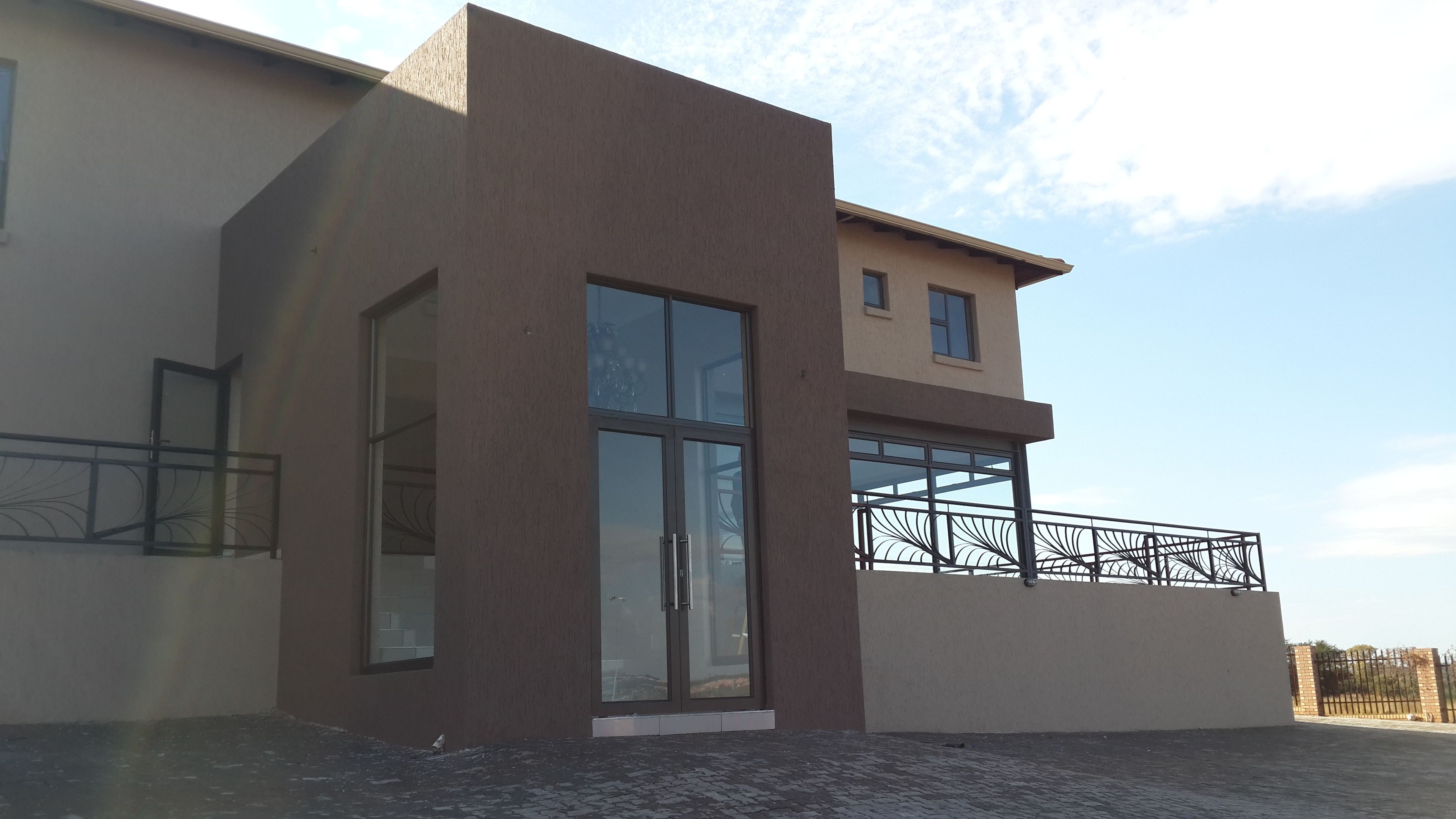 A modern building with a large glass door, a balcony with a metal railing, and a paved ground.