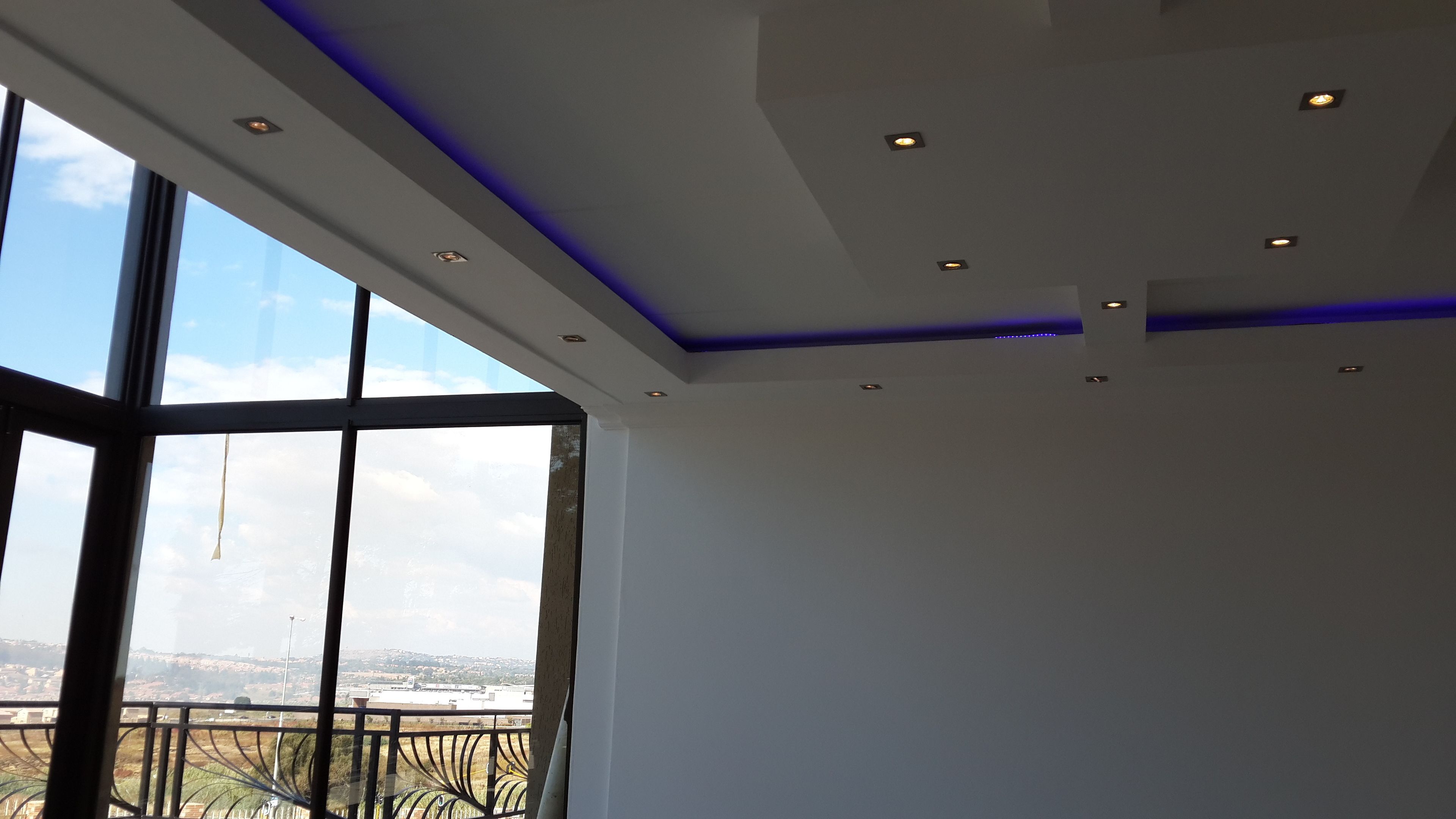 A room with large windows, a view of a cityscape, and a modern ceiling with recessed lighting.