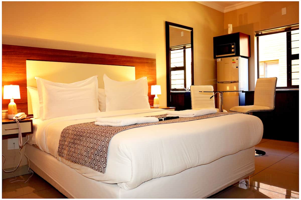A hotel room with a large bed, bedside lamps, a refrigerator, a chair, and a mirror.
