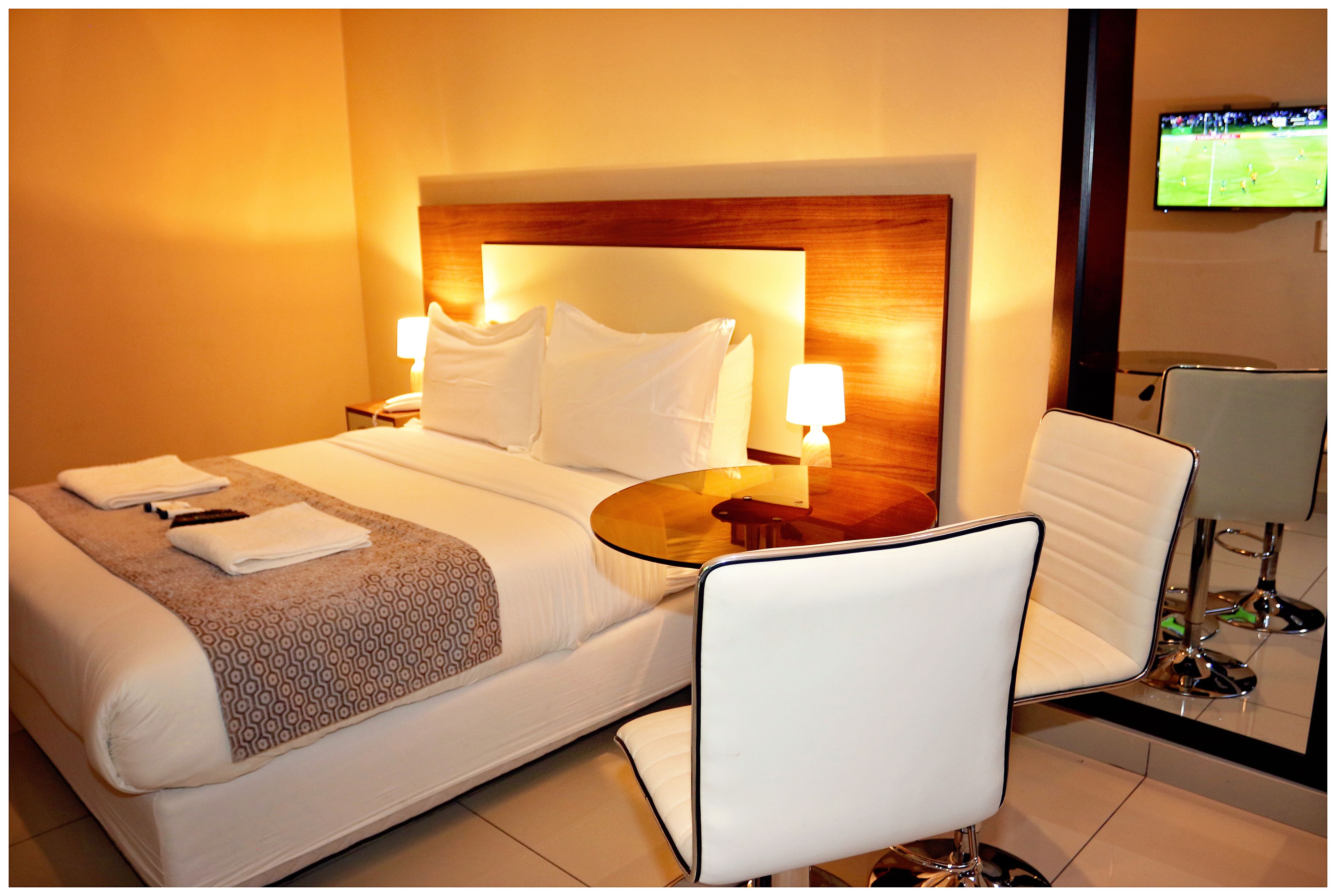 A hotel room with a bed, bedside tables, a chair, and a television on the wall.