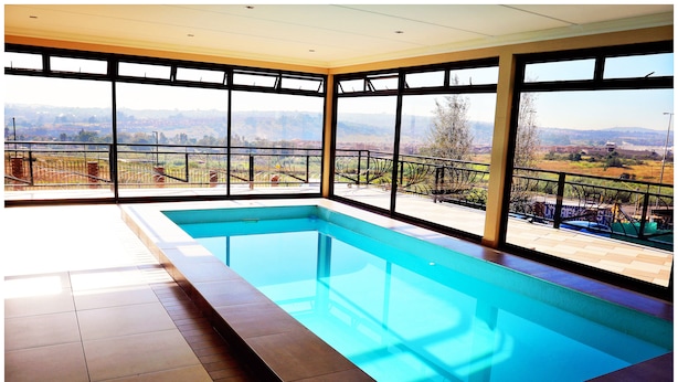 A swimming pool with a view of a distant landscape through large windows. - Eagle Nest Luxury Accommodation (Roodepoort)