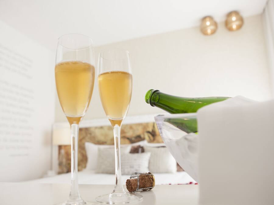 Two champagne flutes on a table with a champagne bottle and a cork.