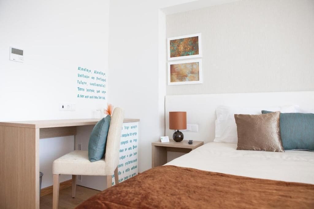 Une chambre d’hôtel avec un lit, un bureau et une chaise. Un mur est décoré d’un texte et de deux tableaux encadrés.