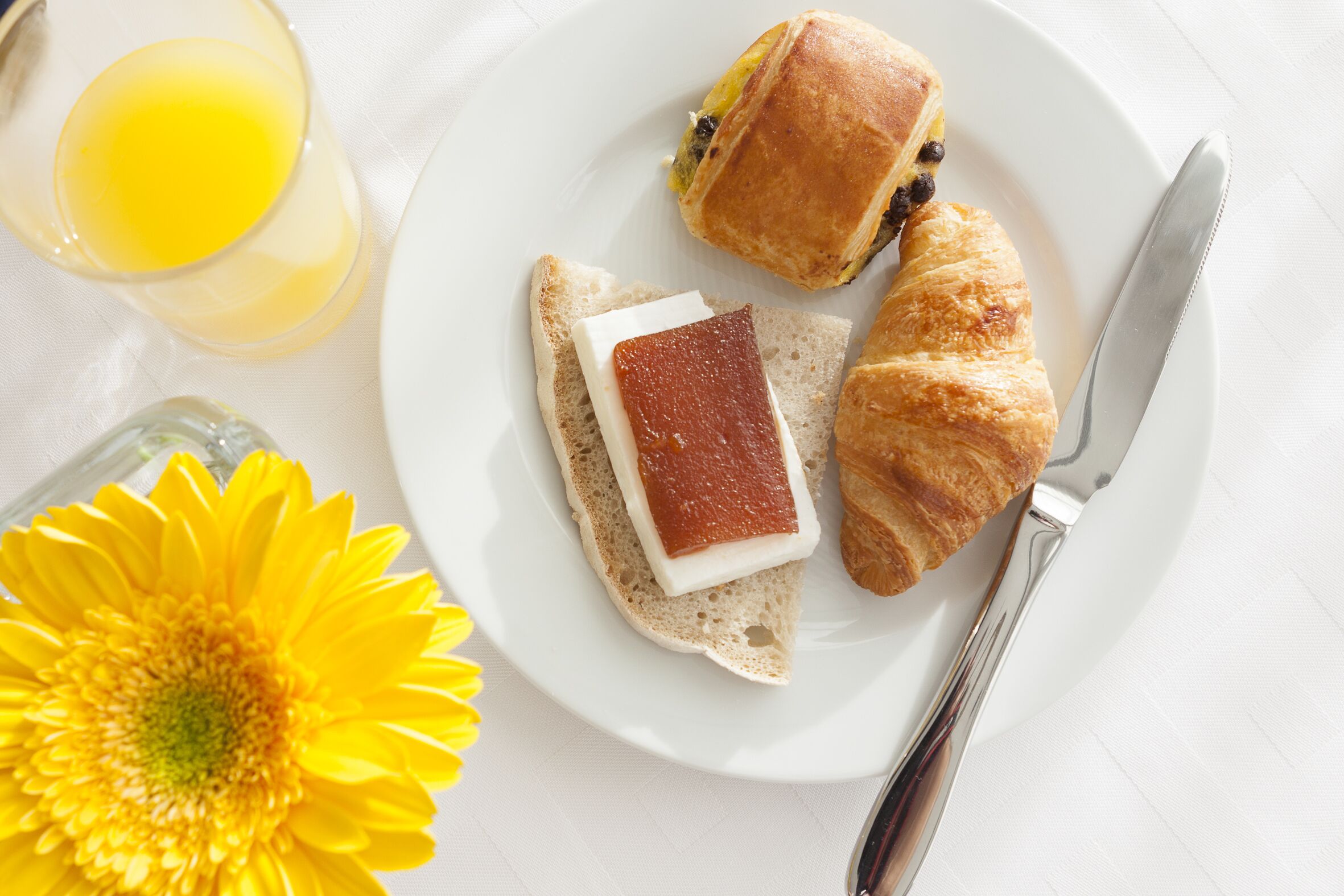A breakfast plate with croissants, a slice of bread with cheese, and a glass of orange juice.