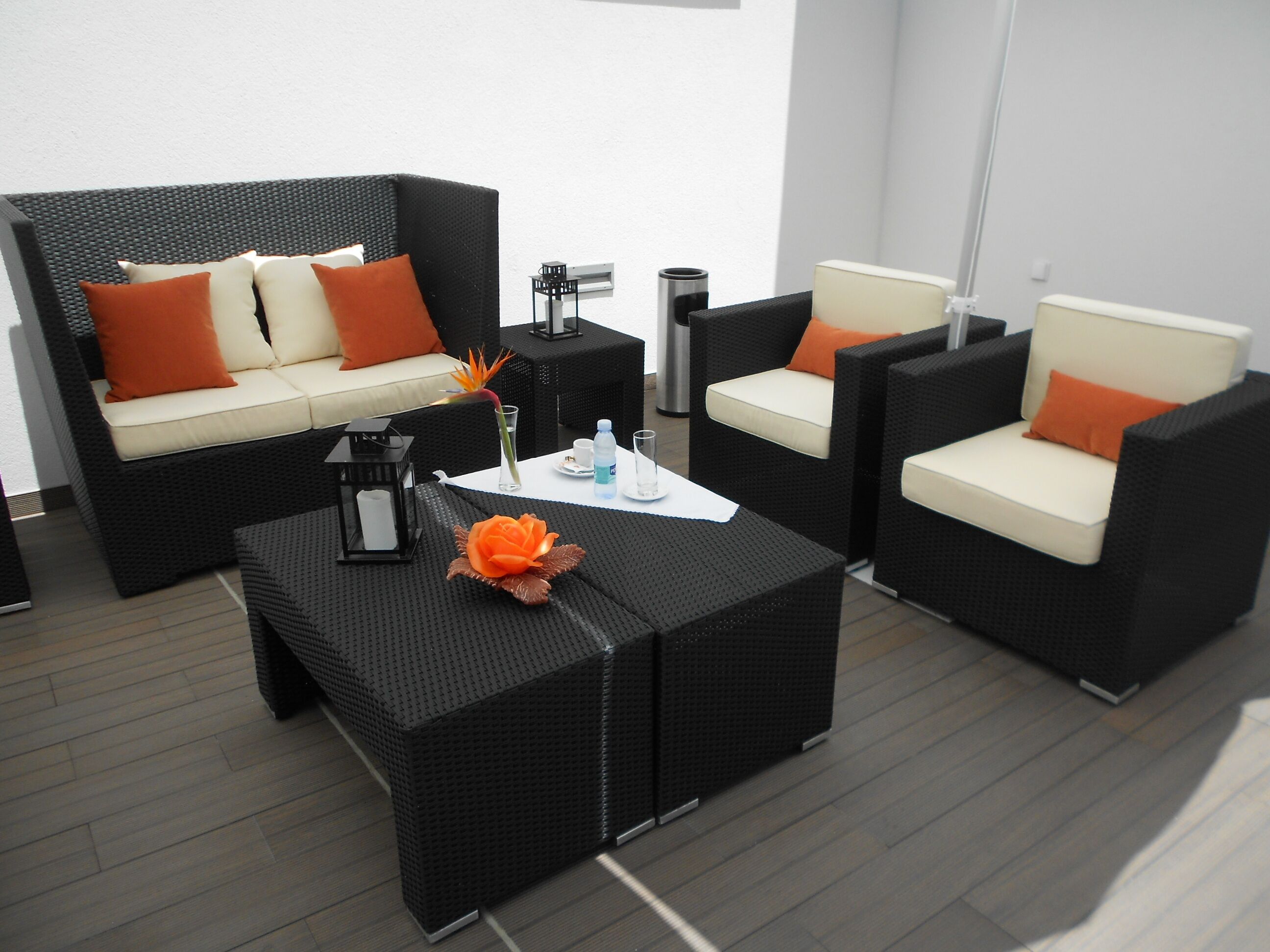 A modern outdoor seating area with wicker furniture, including a sofa and two armchairs, and a small table with a decorative flower centerpiece.