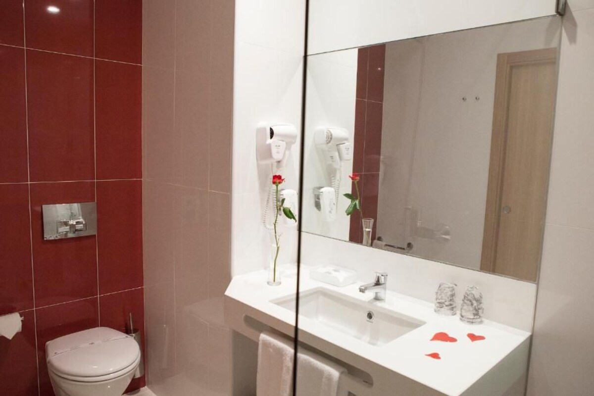 A modern bathroom with a white sink, a mirror, and a red-tiled wall.