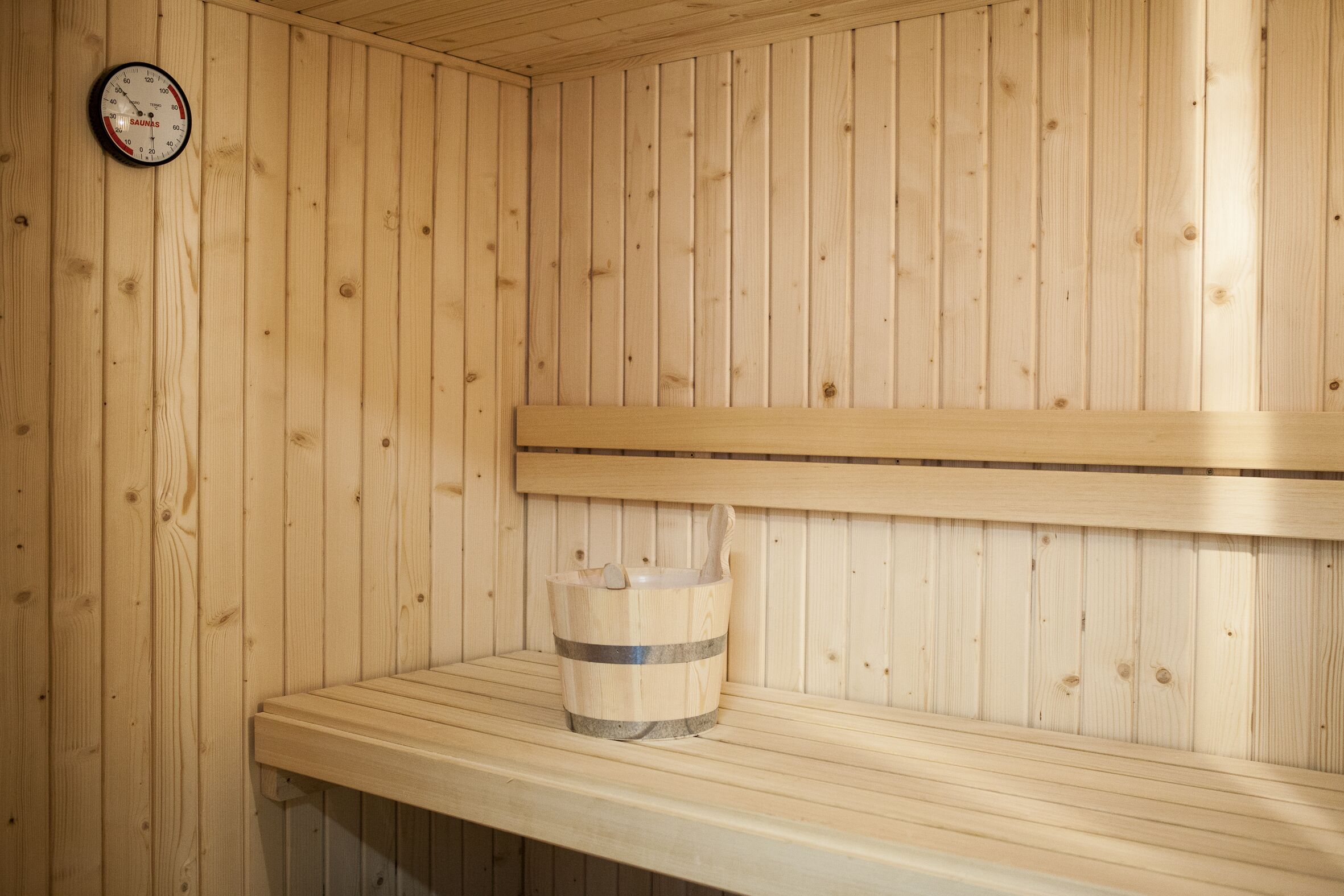 A wooden sauna with a wooden bench and a bucket with a brush.