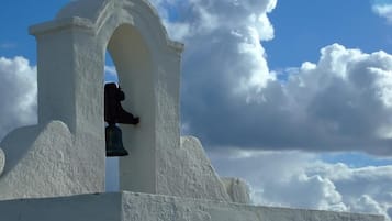 Uma torre de sino branca com um sino, diante de um céu azul e nuvens.