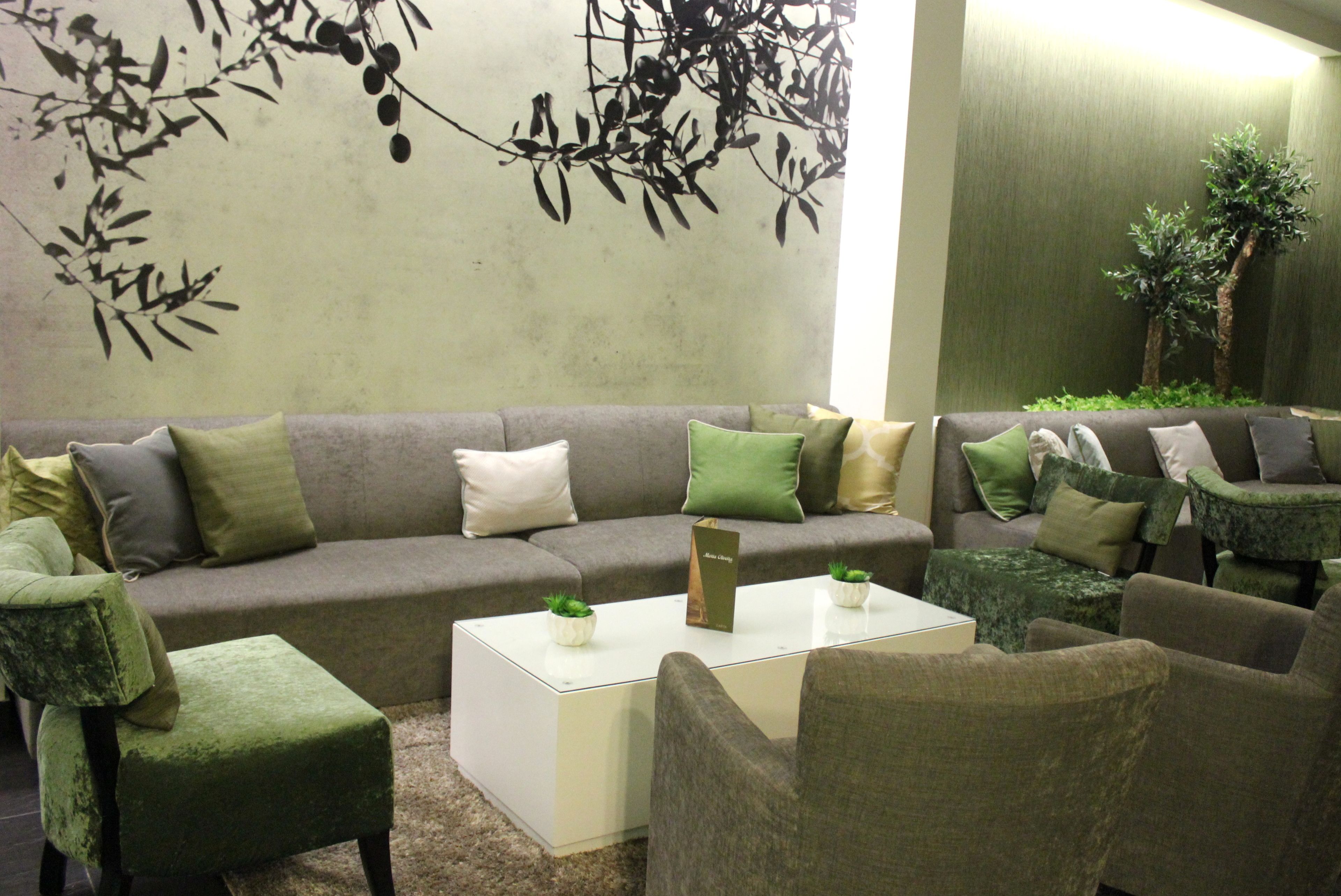 A modern living room with a grey sofa, green and beige cushions, a white coffee table with two small plants, and a green armchair.