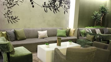 A modern living room with a grey sofa, green and beige cushions, a white coffee table with two small plants, and a green armchair.