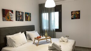 A neatly made bed with white linens, a tray with a bottle and glasses, and towels on the side. - Angela (Chania)