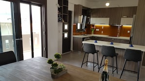A modern kitchen with wooden cabinets, a white countertop, and a bar area with stools. - Angela (Chania)