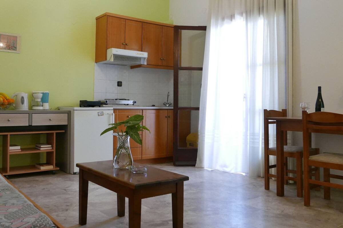 A compact kitchen with wooden cabinets, a small refrigerator, and a dining area with a table and chairs.