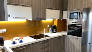 A modern kitchen with wooden cabinets, a stainless steel refrigerator, an oven, and a microwave. - Angela (Chania)