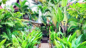 A pathway flanked by lush tropical plants leading to a traditional building with a red roof. - Ban Keaw Villas (Koh Samui)