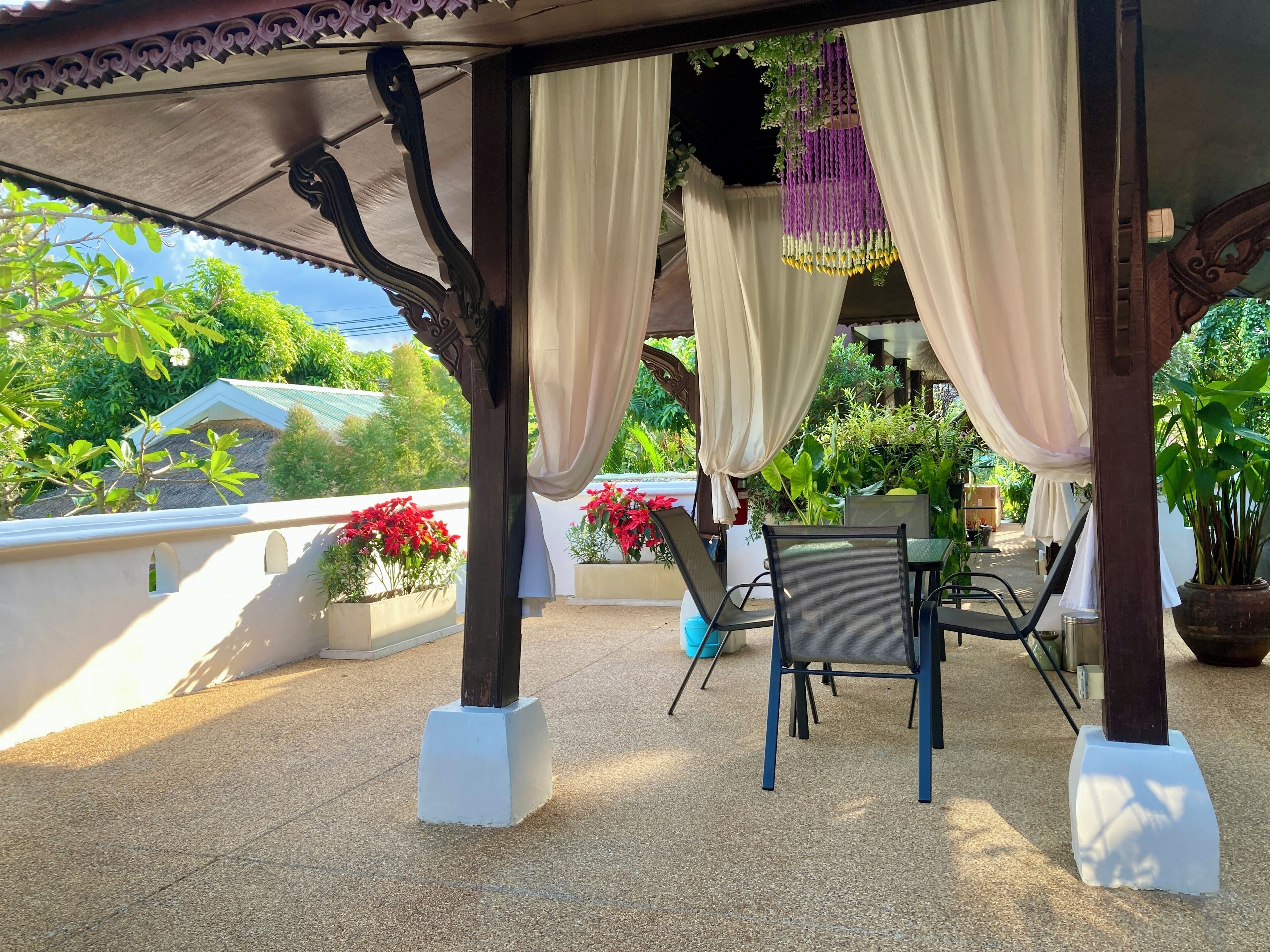 An outdoor patio with a covered seating area, white pillars, and potted plants.