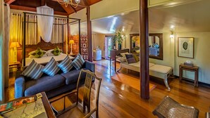A spacious room with a large bed, a sofa, and a wooden floor. There is a window with curtains, a lamp, and a plant. - Ban Keaw Villas (Koh Samui)
