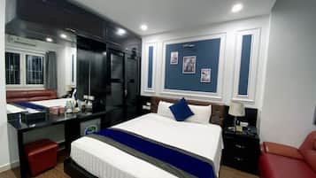 A hotel room with a large bed, a desk, a red chair, a wardrobe, and a mirror.