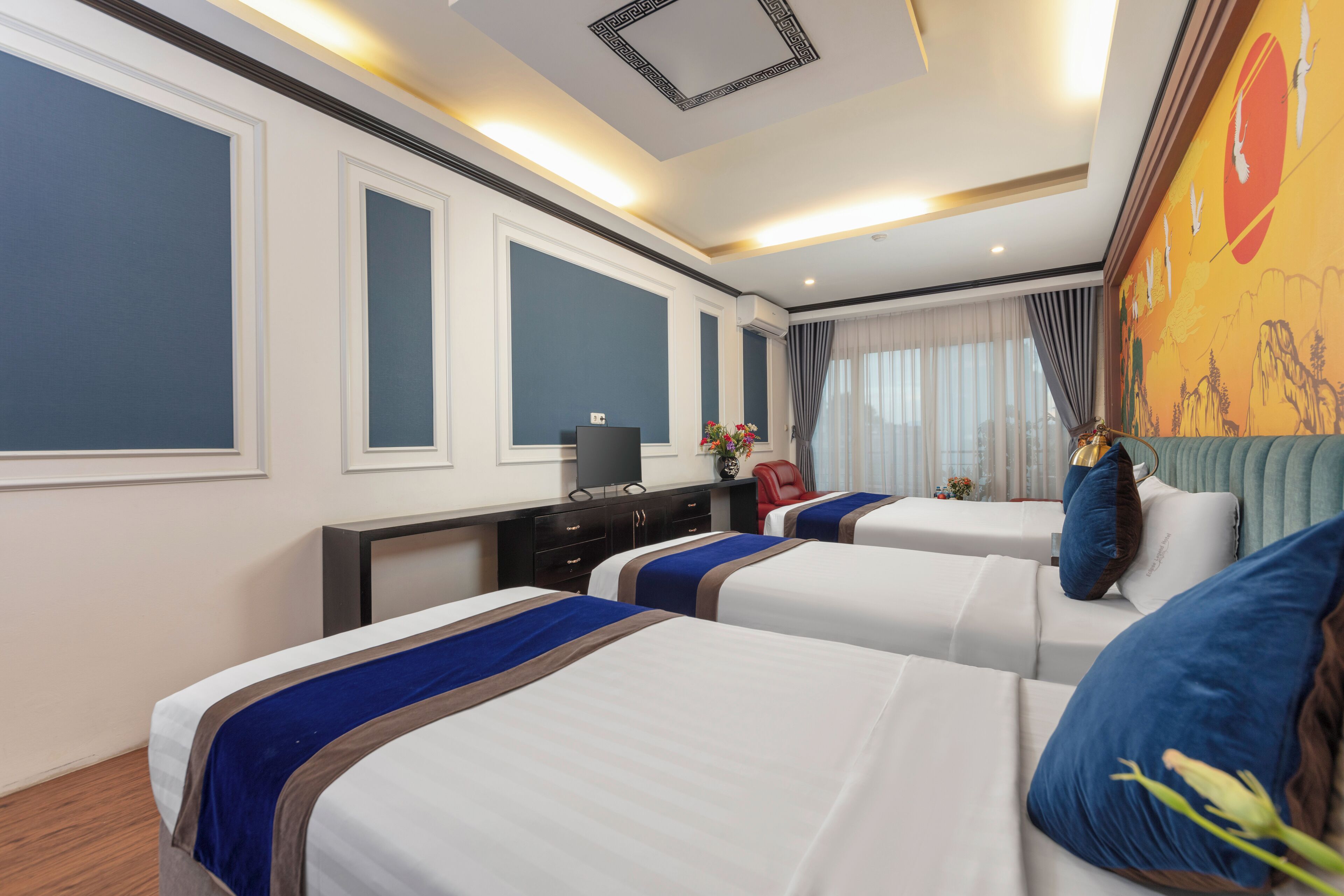 Habitación de hotel con dos camas, un escritorio con computadora, una silla roja y un mural decorativo en la pared.