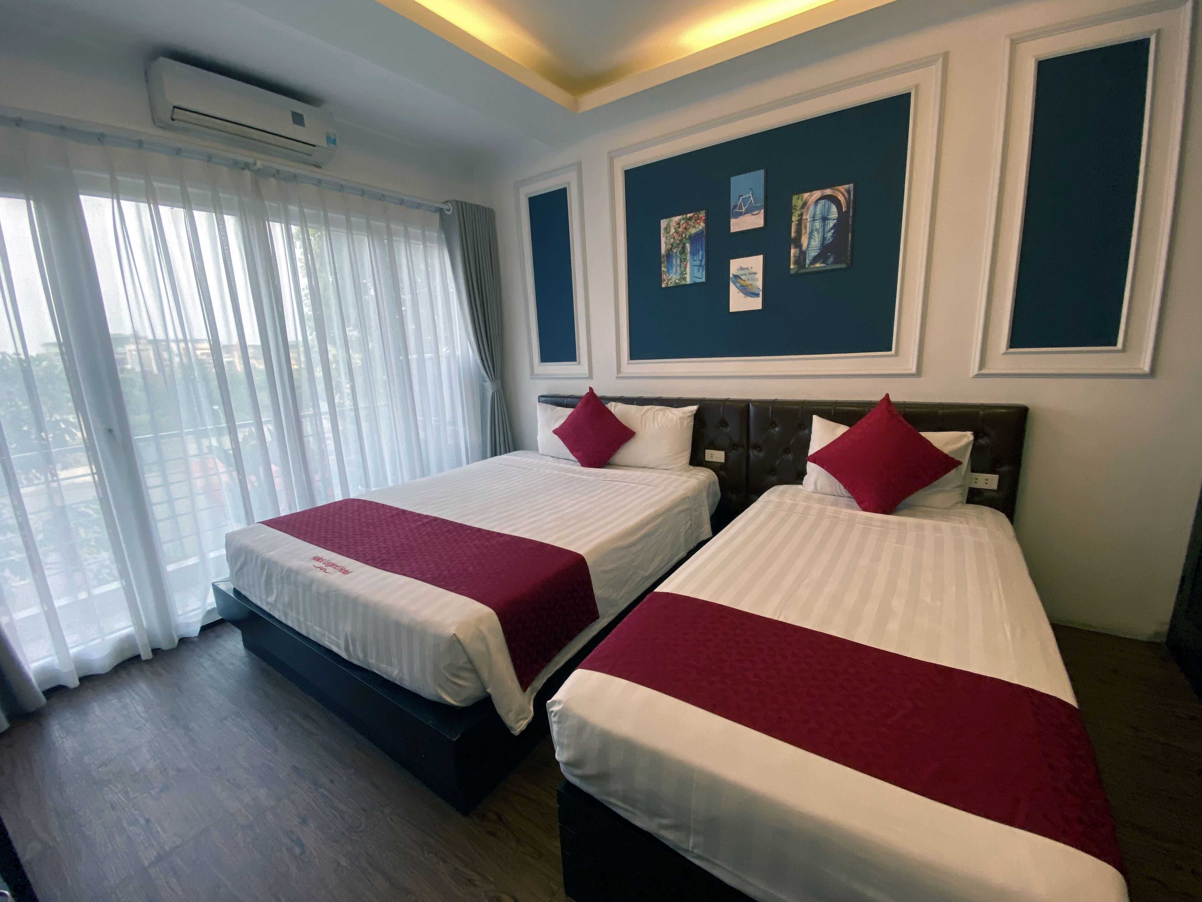 Habitación de hotel con dos camas, un ventanal con cortinas y decoración en la pared.