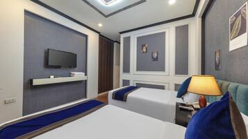 A hotel room with two beds, a TV, a bedside table with a lamp, and artwork on the walls.