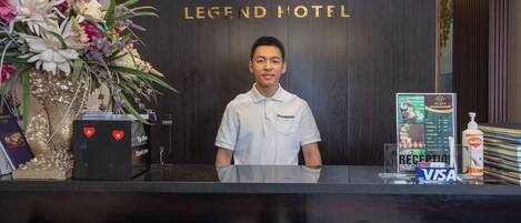 Un mostrador de recepción de hotel con un arreglo floral, un letrero del Hotel Eclipse Legend y un cartel que indica que aceptan tarjetas Visa.