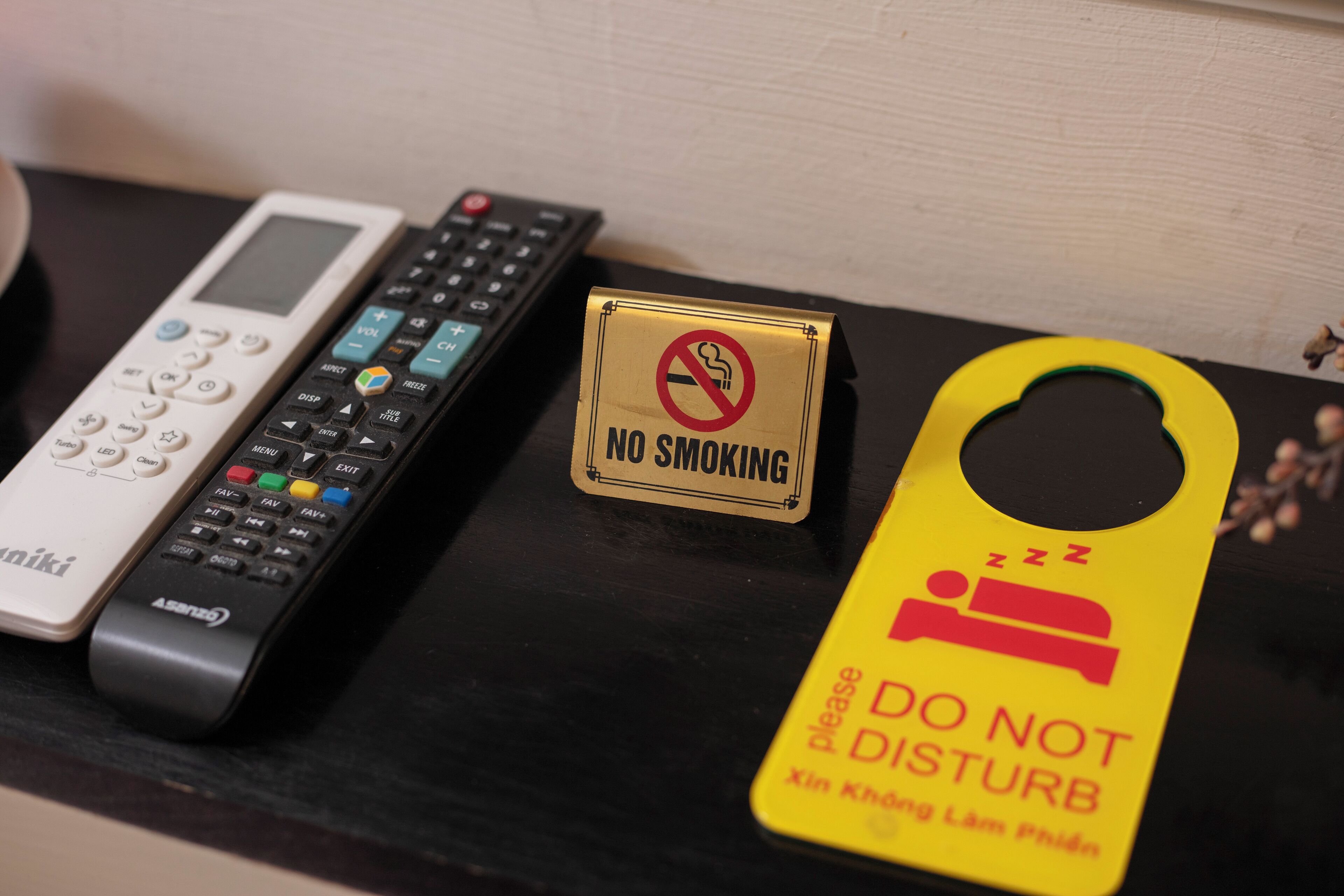 A remote control, a 'No Smoking' sign, and a 'Do Not Disturb' sign on a black surface.