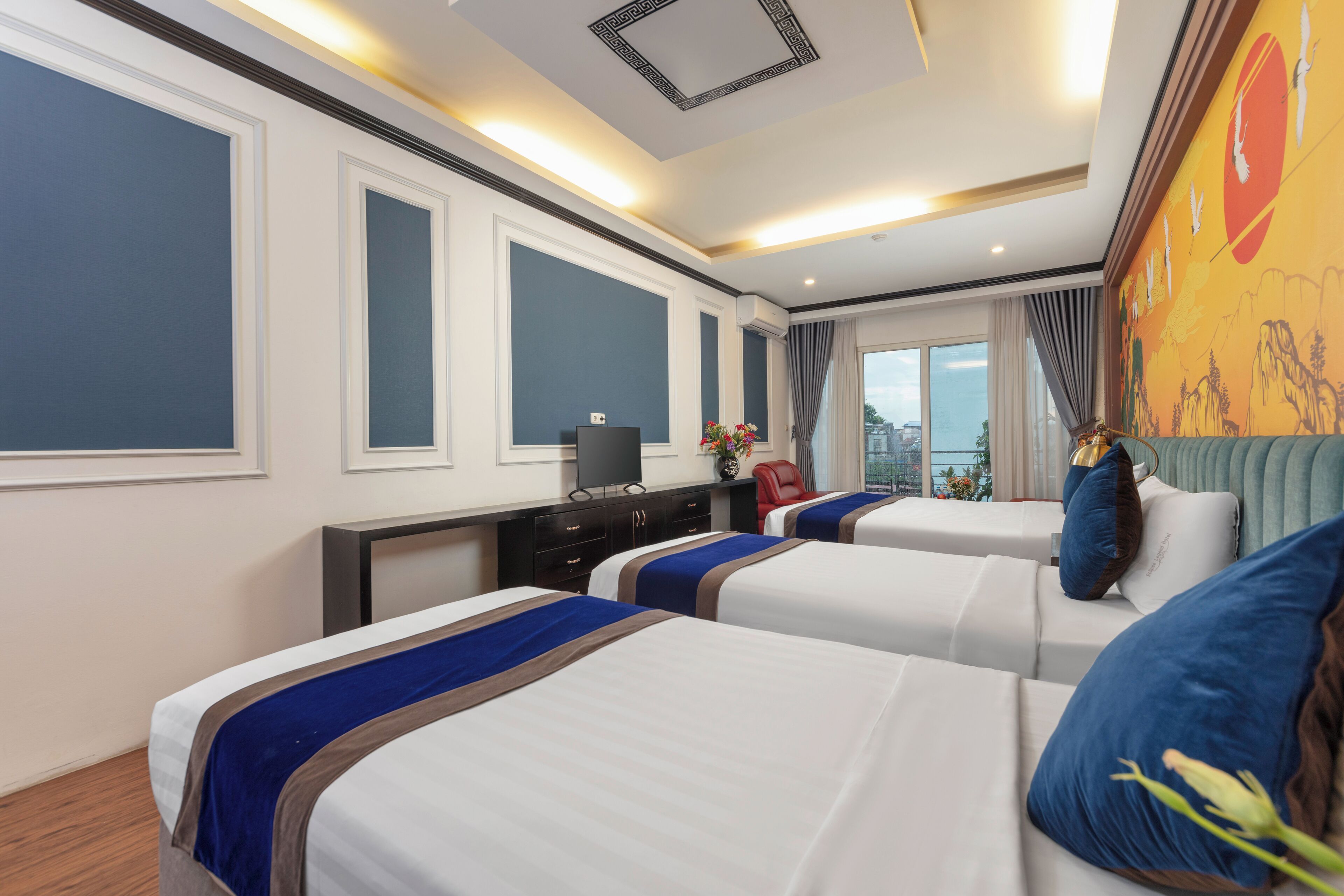A hotel room with two beds, a desk with a TV, and a large window with a city view.