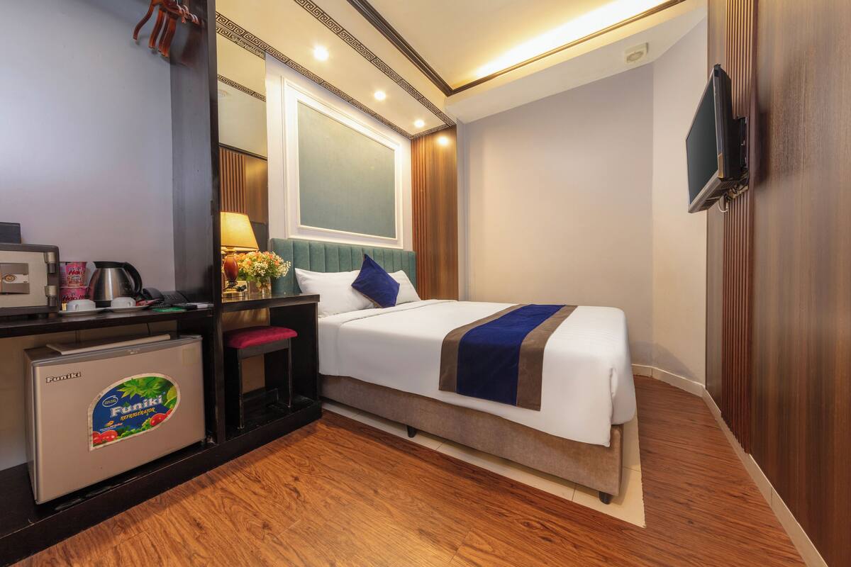 A hotel room with a bed, a desk with a coffee maker, a mini-fridge, and a TV mounted on the wall.