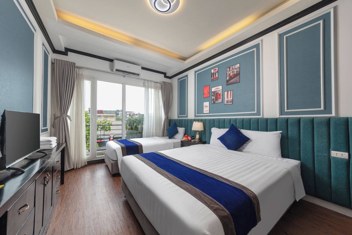 Habitación de hotel con dos camas, televisión, escritorio y ventana con cortinas.