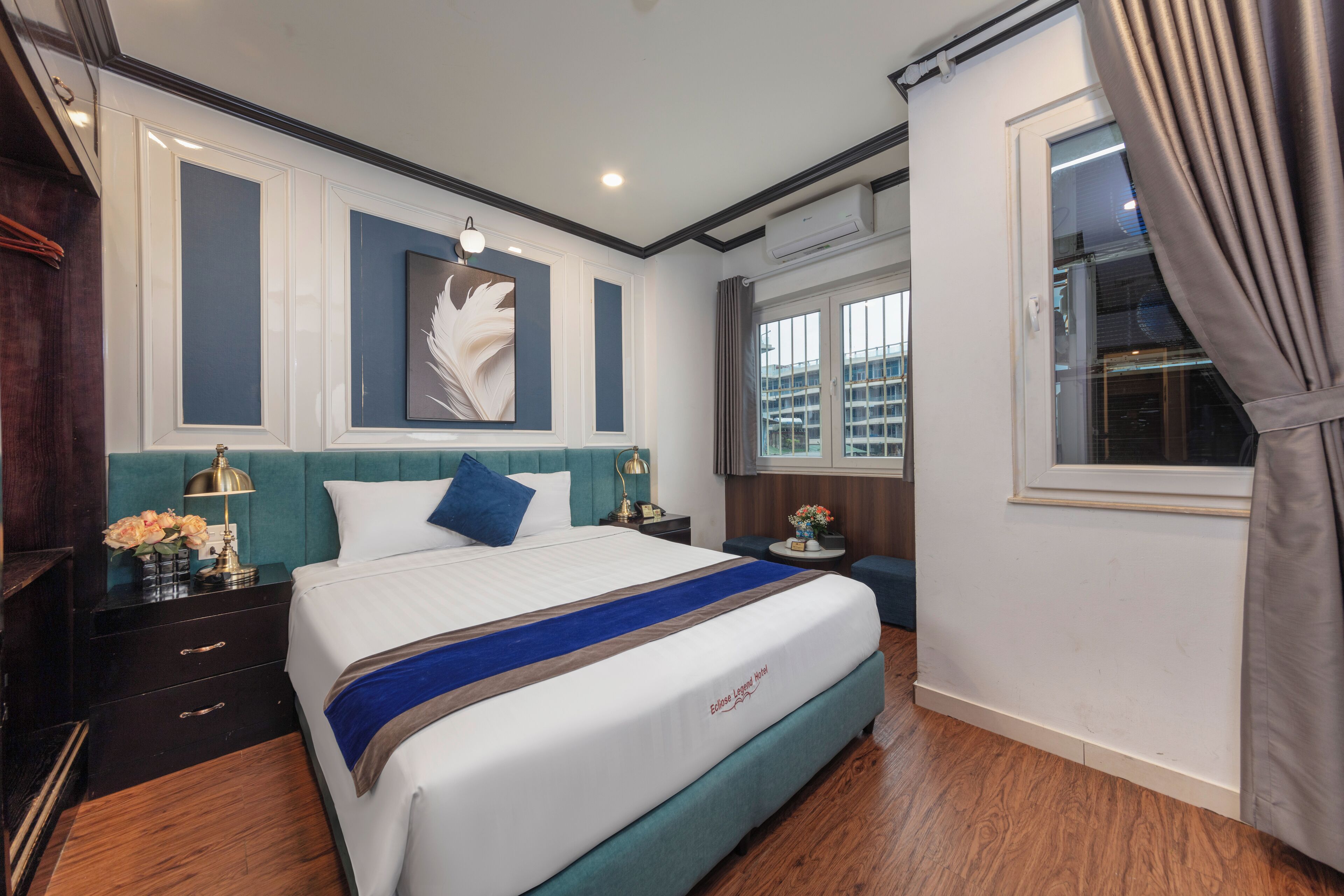 A hotel room with a bed, a nightstand, a lamp, a window with curtains, and a wall-mounted air conditioner.