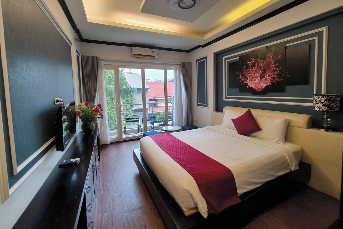 Habitación de hotel moderna con una cama grande, televisión de pantalla plana, escritorio y balcón con vistas a edificios.