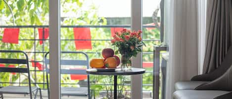 Un balcón con una mesa que sostiene fruta y flores, una silla y vistas a follaje y decoraciones rojas.