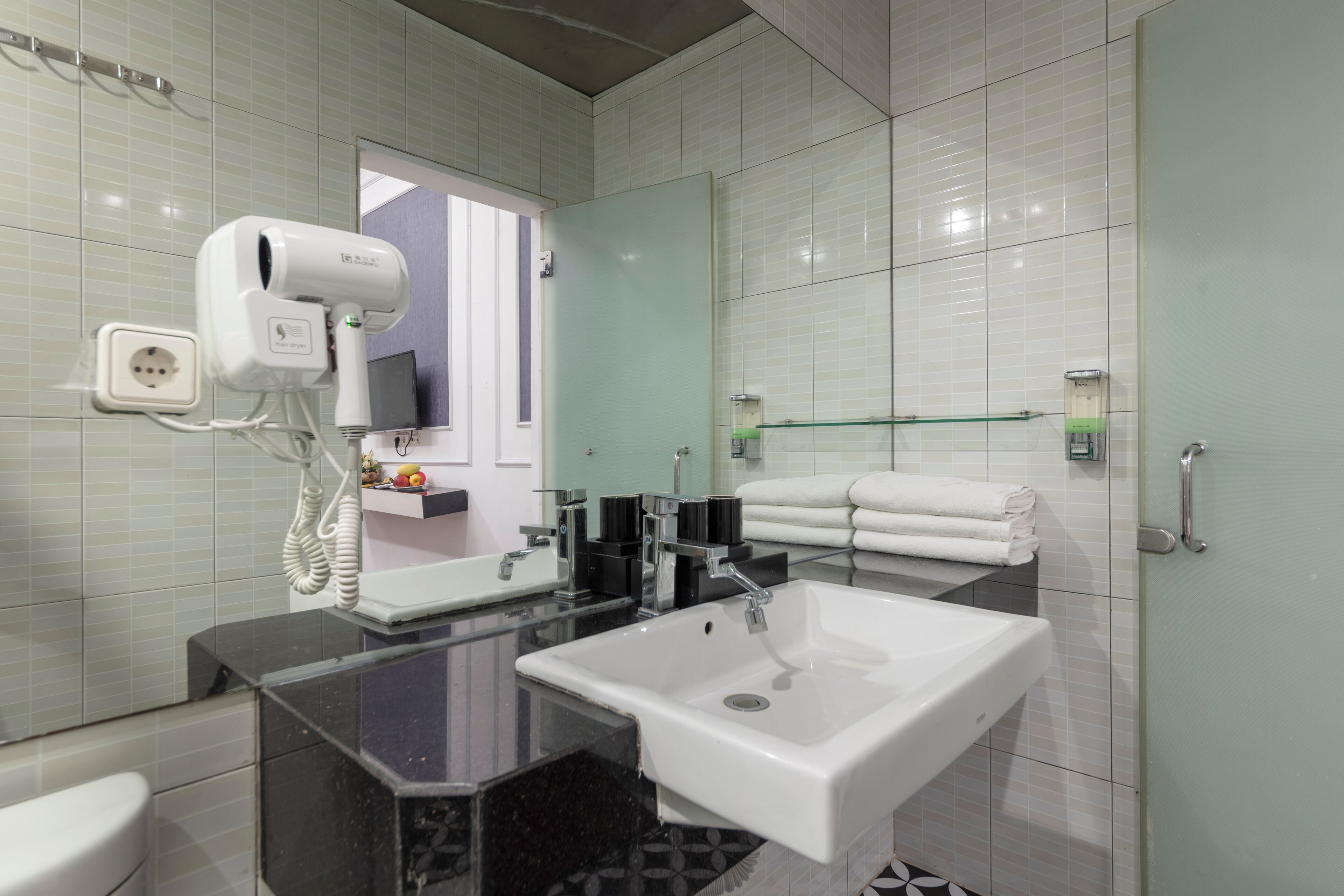 A modern bathroom with a glass-enclosed shower, a white sink, and a hairdryer mounted on the wall.