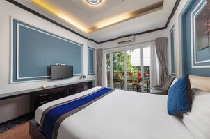 A hotel room with a large bed, a flat-screen TV, a desk, and a balcony with a view of the outside.