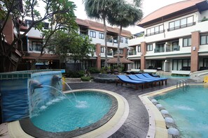A hotel courtyard with two swimming pools, lounge chairs, and a dolphin mural.
